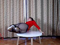 Un'elegante donna matura si spoglia davanti a un tavolo rotondo in collant e tacchi alti. Non perdere questo spettacolo piccante!